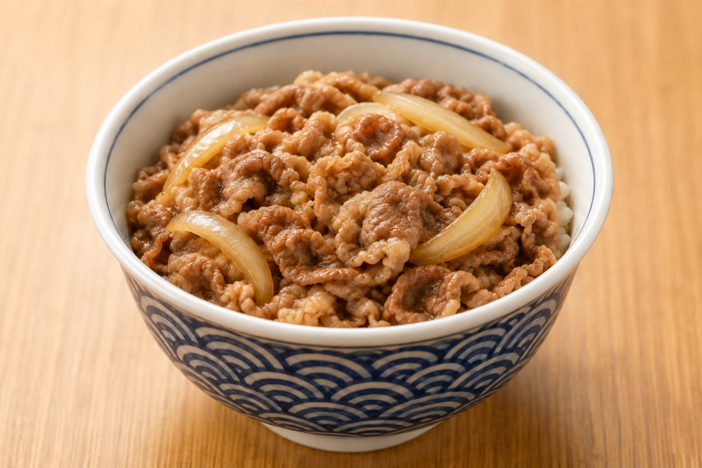 木目のテーブルの上に、青白い波模様の丼に入った牛丼が置かれている。ご飯の上に煮込まれた牛肉と玉ねぎがたっぷり盛られている。